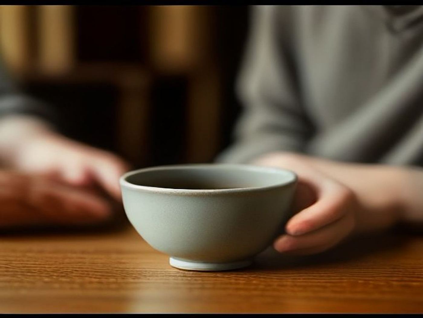 A ceramic bowl on a wood table, two people sitting just out of focus behind it.