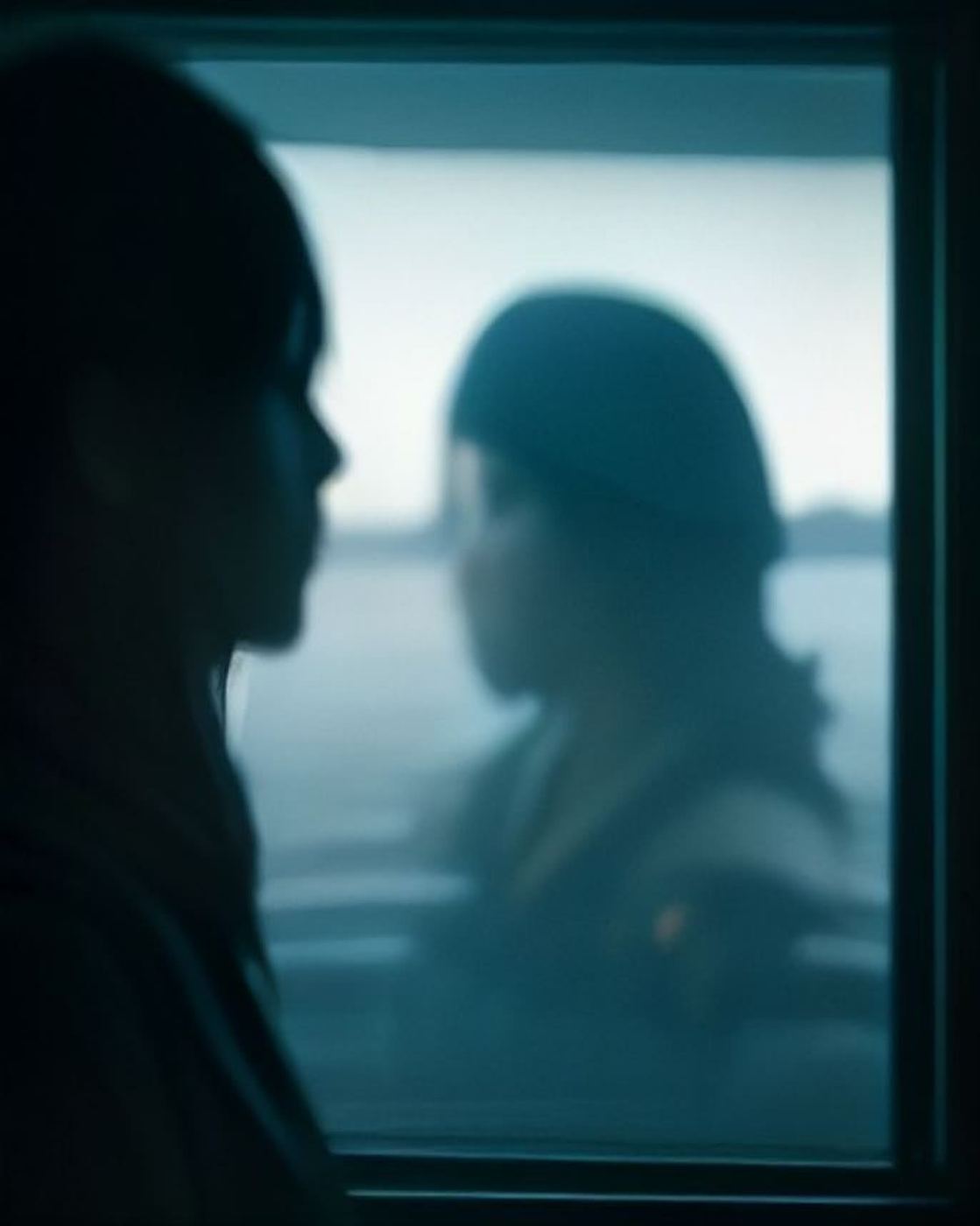 Silhouette of a person looking out a ferry window at grey water.